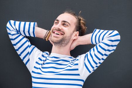 Close up portrait of young man relaxing with hands behind head against black backgroundの写真素材