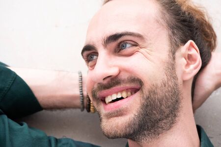 Close up portrait of smiling young man with beard and hands behind headの写真素材