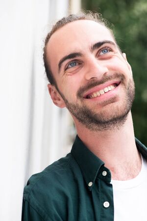 Close up portrait of smiling man with beard leaning against wall outside