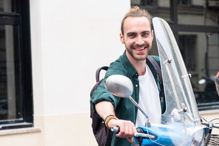Portrait of happy young man with motorbike scooter in city
