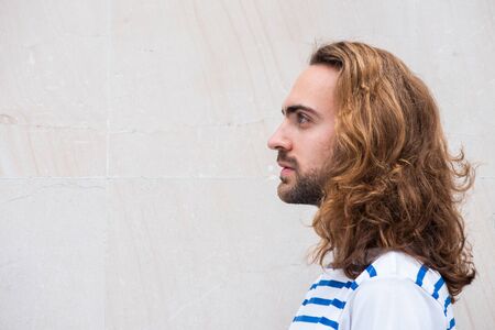 Close up side portrait of young man with long hair and beard by white backgroundの写真素材