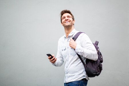 Side portrait of handsome older man walking with bag and mobile phone by gray background