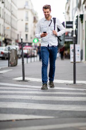 Full length portrait of happy travel man crossing street with mobile phoneの写真素材