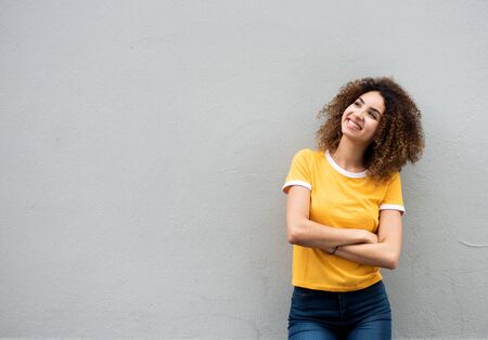 Portrait of cute young woman with curly hair and arms crossed by gray background