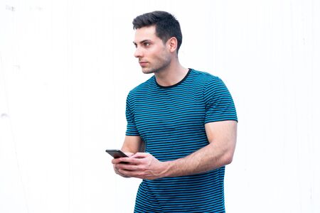 Side portrait of handsome young man holding cellphone by white background