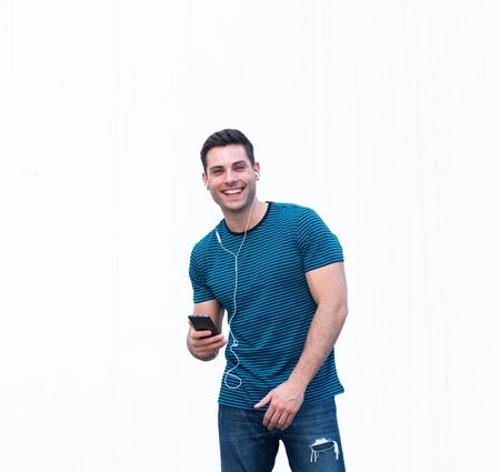 Portrait happy young man listening to music with cellphone and earphones by white background