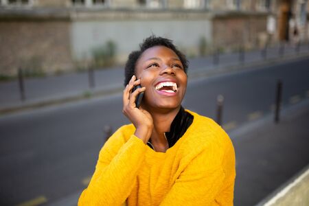 Portrait of young happy african woman talking with cellphone in city