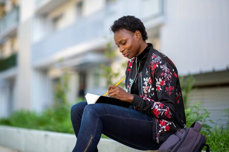 Side portrait young african woman sitting outside with book
