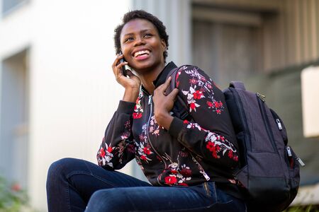 Side portrait happy young african woman sitting with bag talking with mobile phone
