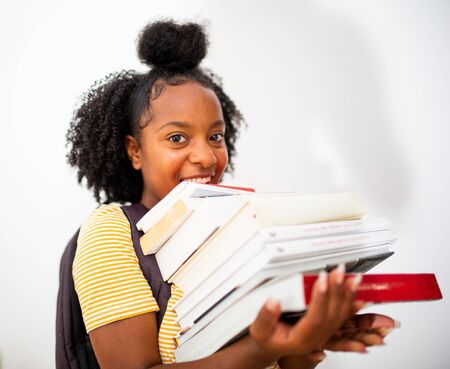 Portrait smiling black teenage girl student holding many books by white background