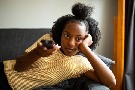 Portrait of african american girl relaxing with tv remote controlの写真素材