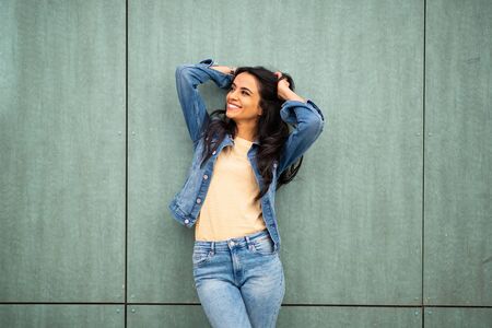 Portrait smiling young woman posing by green wall with hands in hairの写真素材