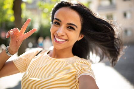 Portrait selfie portrait smiling young hispanic woman with peace hand sign