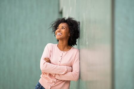 Portrait happy young black woman leaning against green wall with arms crossed