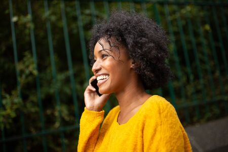 Close up side portrait smiling young black woman talking with cellphone outdoorsの写真素材