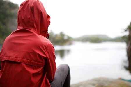 Behind person sitting outside by lake on rainy day