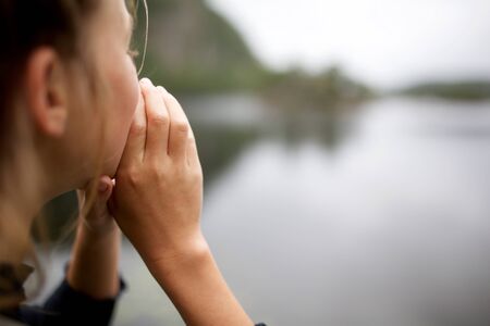 Close up girl shouting by lake with hands to mouth