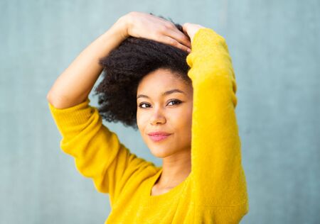 Close up portrait beautiful young african american woman with hand in afro hair by green backgroundの写真素材