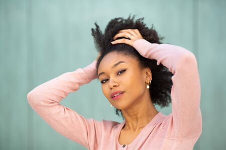 Close up beauty portrait young black woman with hands behind head by green background