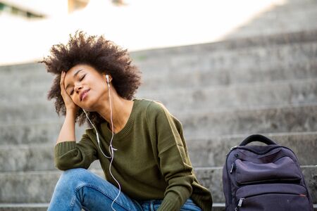 Portrait young black woman sitting on steps outside listening to music with earphonesの写真素材