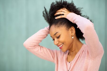 Close up beauty portrait smiling young black woman with hands behind head by green backgroundの写真素材