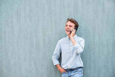 Portrait happy young man talking with mobile phone by wallの写真素材
