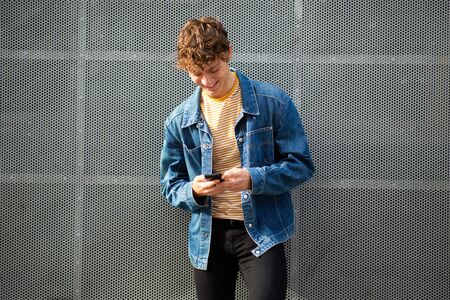 Portrait of smiling young man looking at mobile phone by gray wall