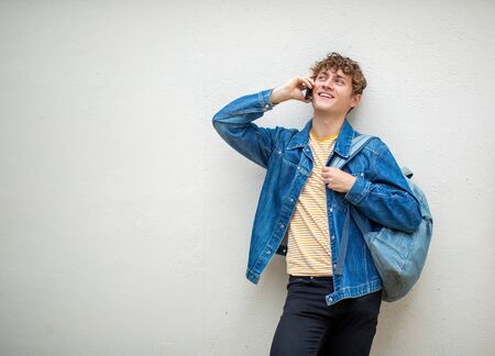 Portrait happy guy with bag talking with mobile phone by wall