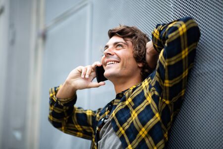 Close up smiling man leaning against wall talking with mobile phone