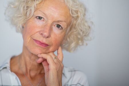 Close up portrait attractive older woman against white background with hand to face