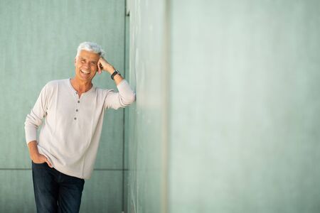 Portrait handsome older man leaning against green wall and smiling