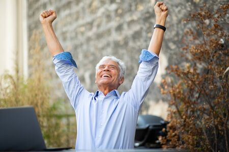 Portrait happy older man cheering with arms raisedの写真素材