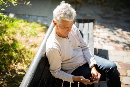Portrait senior man sitting on park bench looking at cellphoneの写真素材