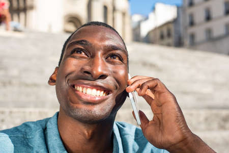 Close up portrait smiling young black man talking with cellphone outside and looking upの写真素材