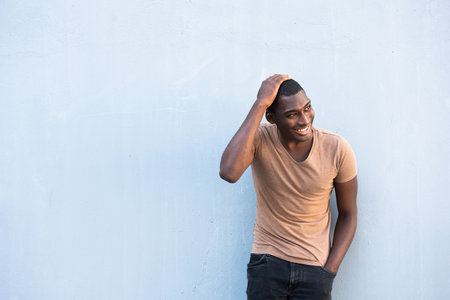 Portrait smiling young black man against gray wall and hand on headの写真素材