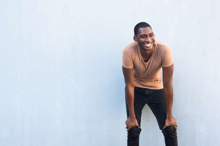 Portrait happy young black man with hands on knees by gray background