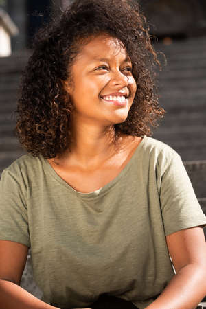 Close up portrait attractive young woman with curly hair sitting outside and looking away