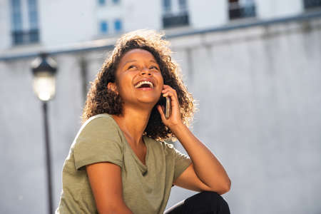 Close up portrait beautiful young woman laughing while talking with mobile phone outsideの写真素材