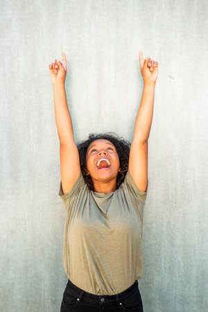Portrait happy young African American woman with arms raised and fingers pointing upの写真素材