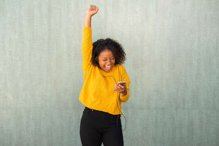 Portrait cheerful young African American woman using mobile phone to listen to music with headphonesの写真素材