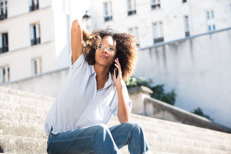 Portrait young woman with eyeglasses sitting outside talking on cellphoneの写真素材