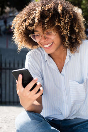 Close up portrait smiling african American teen girl with eyeglasses looking at mobile phone