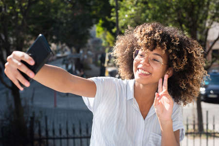 Portrait smiling young black woman taking selfie photo with mobile phoneの写真素材