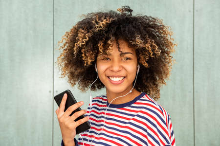 Close up portrait happy African American girl listening to music with phone and earphones