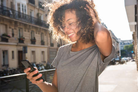 Portrait smiling black girl looking at cellphone in city