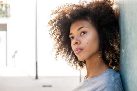 Close up side portrait serious african American girl leaning against wall outsideの写真素材