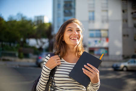 Close up portrait smiling female student with bag and book in city