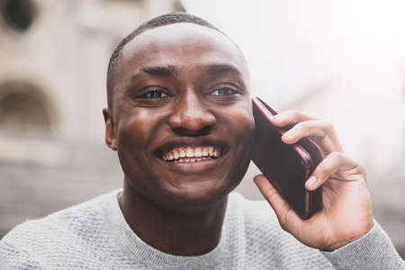 Full length portrait happy African american male traveler walking on street with cellphone and suitcaseの写真素材