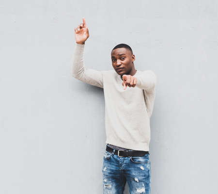 Portrait African american man using mobile phone while standing next to white wall with bag and...