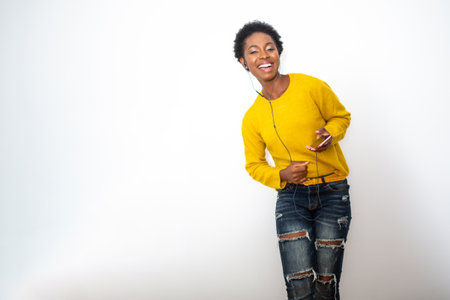Portrait happy African American young woman listening to music with mobile phone and earphonesの写真素材